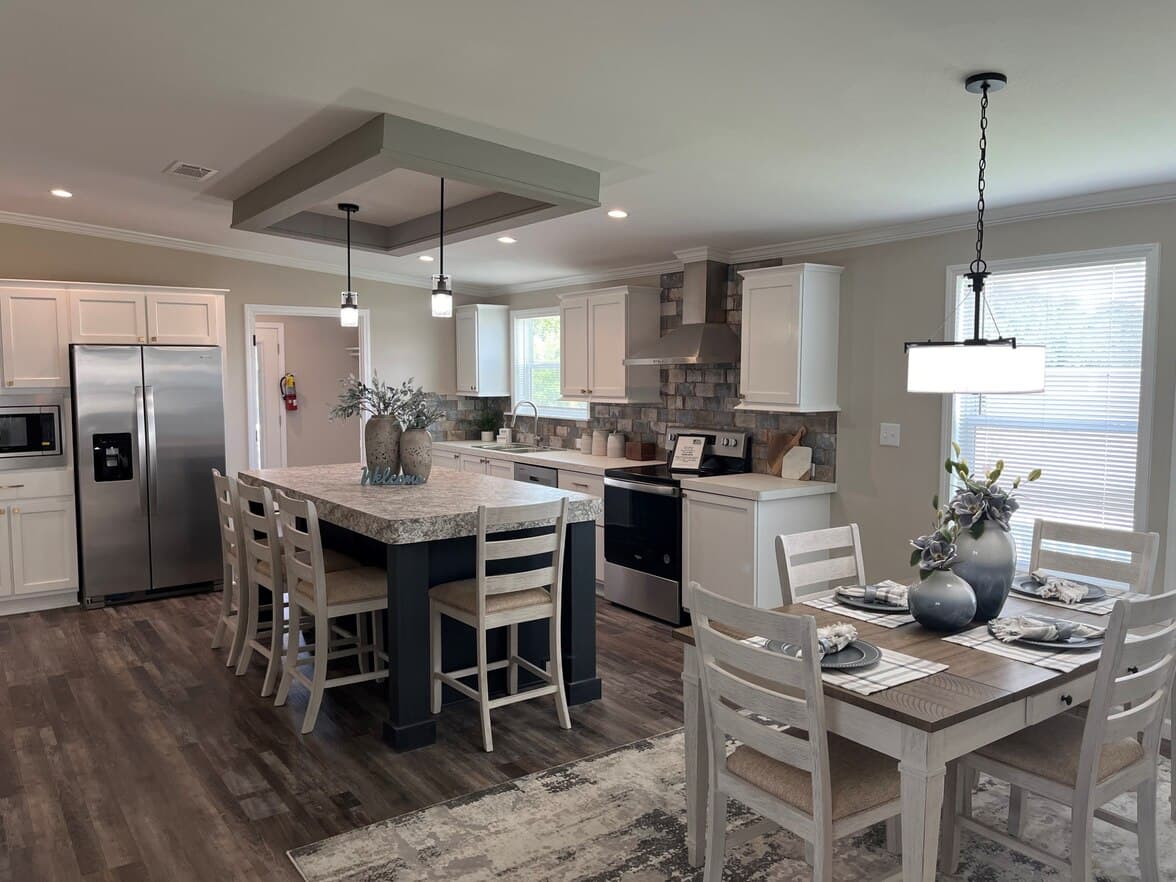 Open-plan kitchen and dining area — large island with bar-stool seating, stone backsplash, stainless appliances, white cabinetry, pendant lights, formal dining set, and wood-look flooring