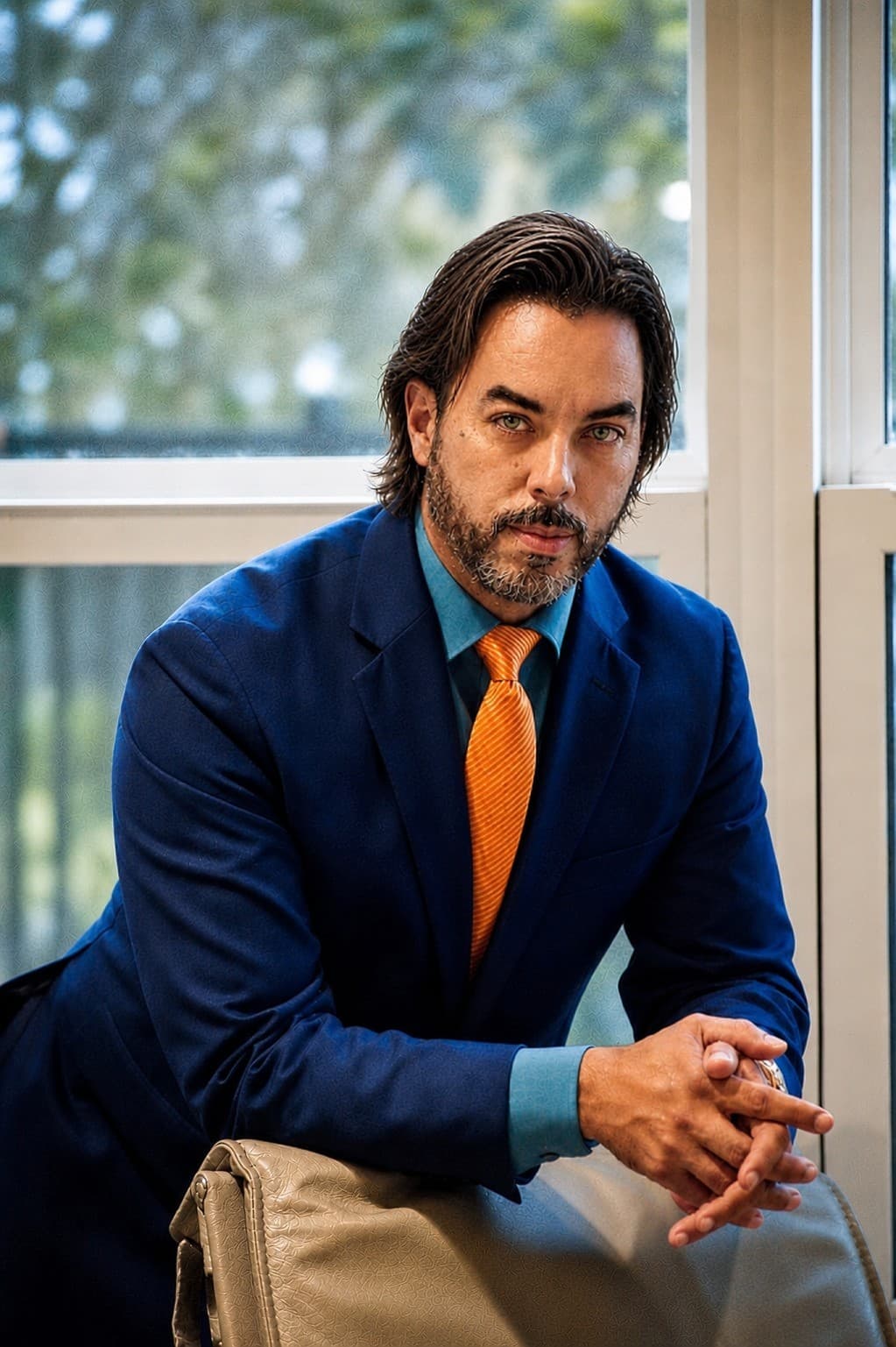 Hector Colon Arias — Founder and CEO of Innova LDP, in a navy suit with teal shirt and orange tie, seated by a window with soft natural light